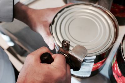 Cropped image of person using can opener at home