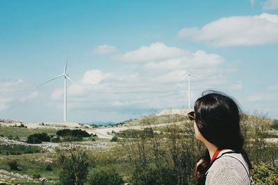 Side view of woman standing against windmills on landscape