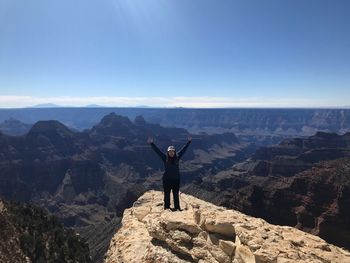 Full length of hiker with arms raised standing on mountain against sky