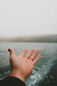 Cropped image of hand at sea against sky