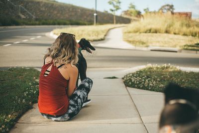 Rear view of young woman sitting with dog on footpath