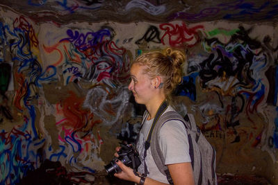 Woman holding camera against graffiti wall