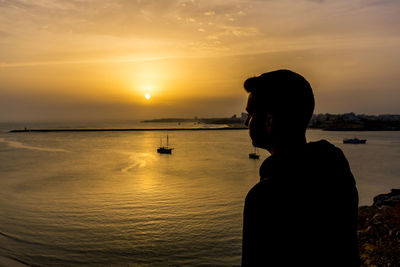 Silhouette man fishing in sea against sunset sky