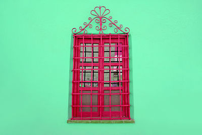 Raspberry red wrought iron vintage window on mint green colored wall