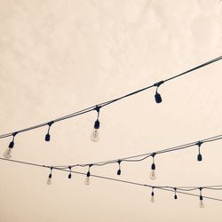 Low angle view of light bulbs hanging against sky