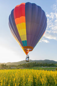 Yellow hot air balloon flying over field against sky