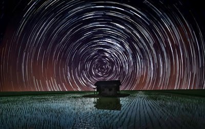 Star trail over abandoned wooden house in the middle of paddy field.