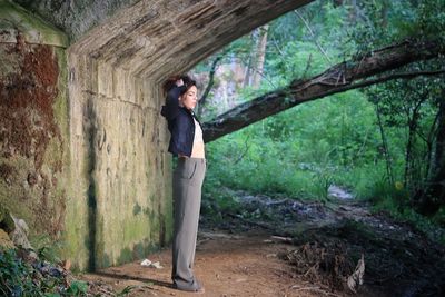 Side view of man standing by tree trunk in forest