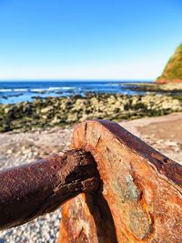 Close-up of rusty metal on beach against clear sky