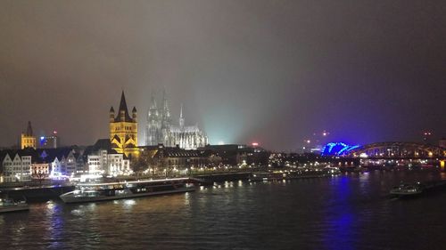 Illuminated cityscape by rhine river against sky at night