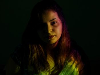Close-up portrait of young woman against black background