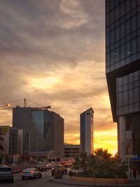 City street by buildings against sky during sunset