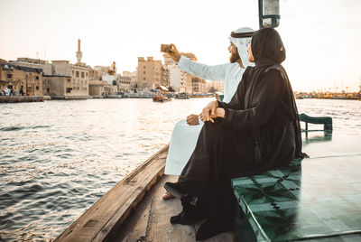 Couple talking selfie while sitting in boat on river during sunset