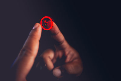 Close-up of hand holding red light over black background