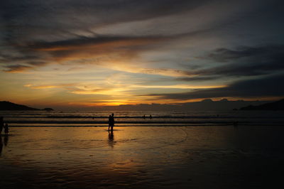 Silhouette person standing on beach against sky during sunset