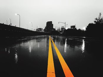 Wet road by city against sky during rainy season
