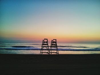 Lifeguard towers at beach against clear sky during sunset