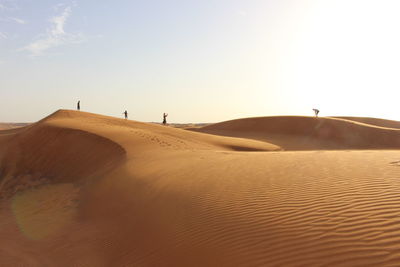 People standing in desert against sky on sunny day