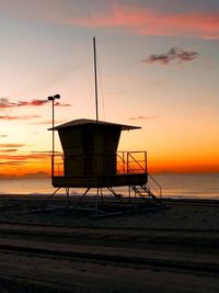 Lifeguard hut on beach against sky during sunset