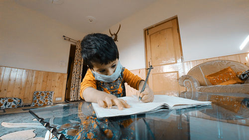 Boy wearing mask writing in book