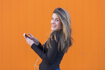 Portrait of smiling woman standing against orange wall