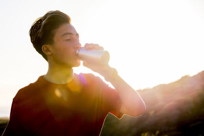 Teenage boy drinking water from bottle outdoors on sunny day