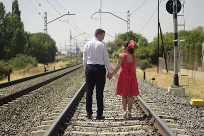 Rear view of couple walking on railroad tracks