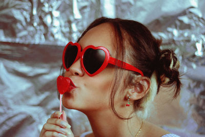 Woman wearing heart shape sunglasses kissing lollipop