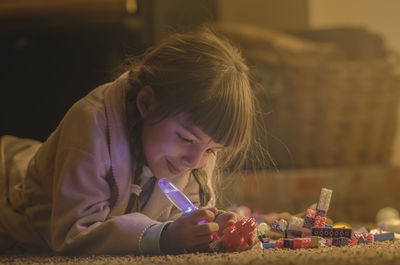 Smiling girl playing with toys while lying on rug at home