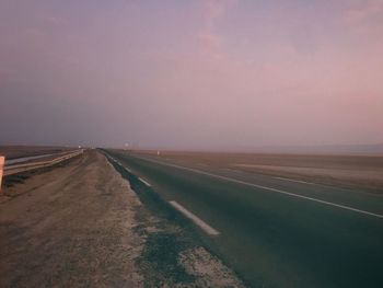 Empty road amidst land against sky during sunset