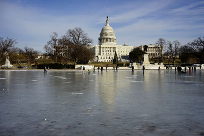 Low angle view of historic capitol, people walking on frozen reflecting pool