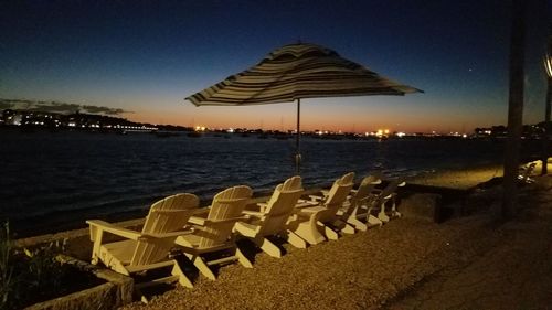 Chairs on beach by sea against sky during sunset