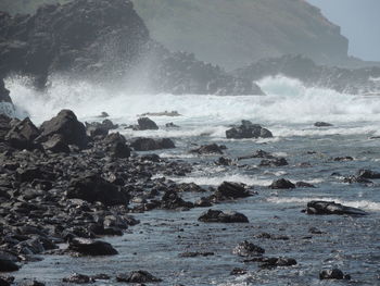 Waves splashing on rocks against clear sky