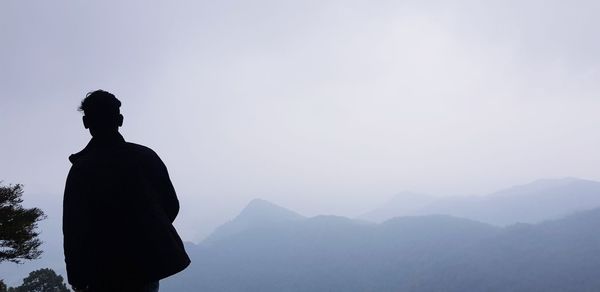 Rear view of silhouette man looking at mountains against sky