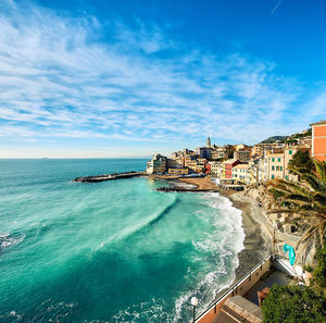 Scenic view of sea by buildings against cloudy blue sky