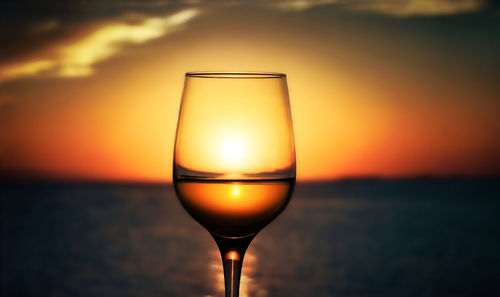 Close-up of wineglass against sea during sunset