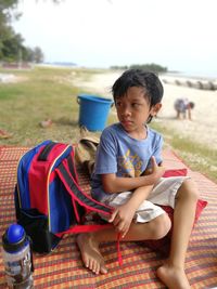 Boy sitting on field against sky