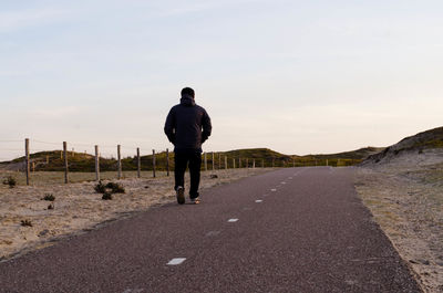 Rear view of man walking on road against sky