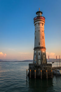 Lighthouse by sea against sky during sunset