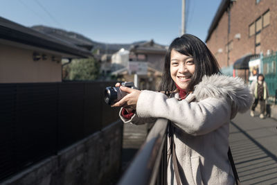 Portrait of young woman photographing against sky in winter