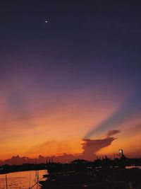 Silhouette buildings by sea against romantic sky at sunset