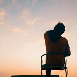 Rear view of silhouette man sitting on seat against sky