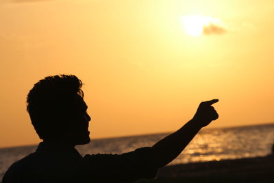 Silhouette man pointing by sea against sky during sunset