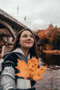 Young woman looking away while standing against sky during autumn