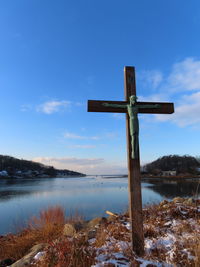 Cross on shore by lake against sky