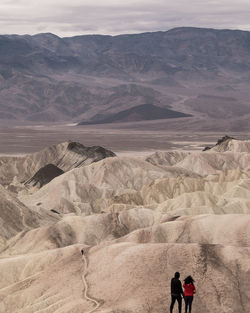 Rear view of people standing at desert against mountains