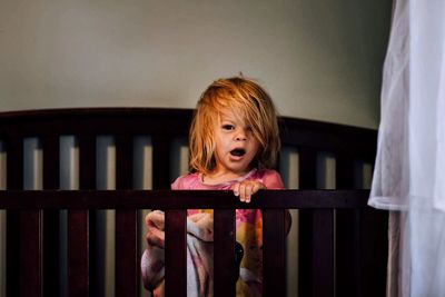 Portrait of girl standing in crib at home