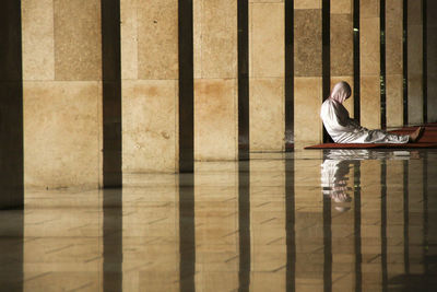 Person leaning on wall in passage with reflection on floor