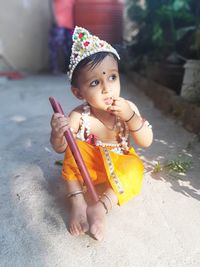 Cute baby boy wearing krishna costume while sitting on footpath