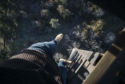 Low section of man climbing down on ladder over trees